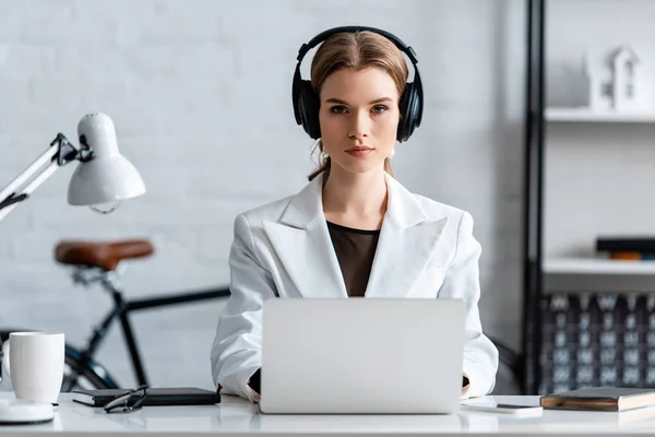 Serious businesswoman in headphones sitting at computer desk at workplace — Stock Photo