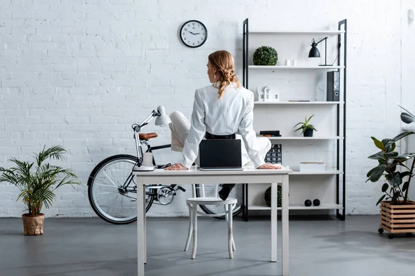 Vista posteriore della donna d'affari in abito formale seduta sulla scrivania del computer in ufficio moderno — Foto stock