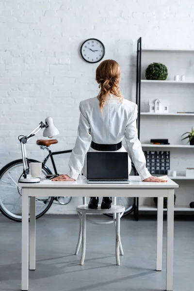 Back view of businesswoman in formal wear sitting on computer desk in office — Stock Photo