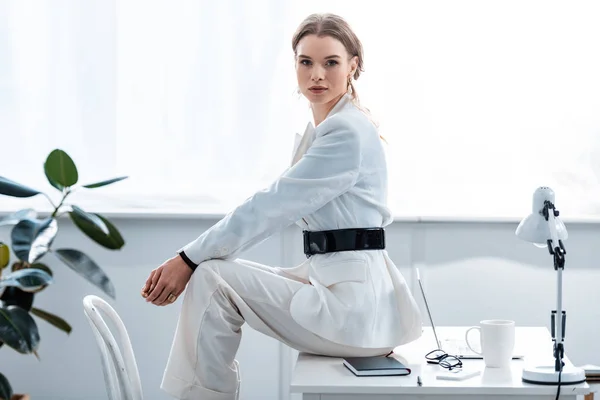Trendige Geschäftsfrau in formeller Kleidung, die am Schreibtisch sitzt und am Arbeitsplatz in die Kamera blickt — Stockfoto