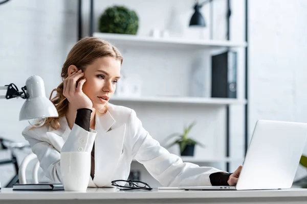Втомлена бізнес-леді в білому формальному одязі сидить за столом і використовує комп'ютер на робочому місці — стокове фото