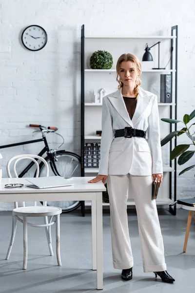 Ernsthafte Geschäftsfrau in weißer formaler Kleidung blickt in moderne Büroeinrichtung in die Kamera — Stockfoto
