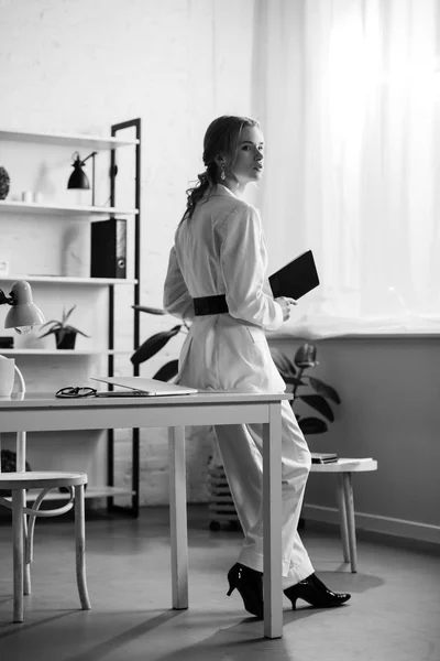 Черно-белое фото деловой женщины в формальной одежде, держащей ноутбук в офисе — стоковое фото