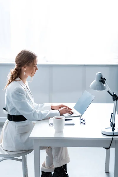 Femme d'affaires en tenue de cérémonie assise au bureau et tapant sur ordinateur portable sur le lieu de travail avec espace de copie — Photo de stock