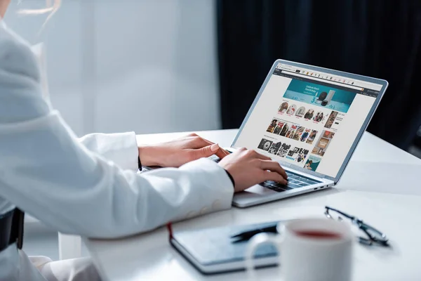 Vista cortada da mulher usando laptop com site amazon na tela na mesa de escritório — Fotografia de Stock