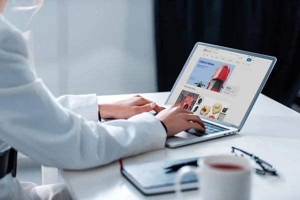 Vista recortada de la mujer usando el ordenador portátil con el sitio web de ebay en la pantalla en el escritorio de la oficina - foto de stock