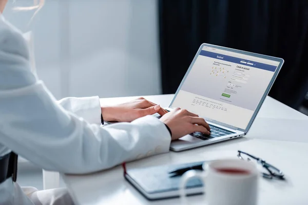 Cropped view of woman using laptop with facebook website on screen at office desk — Stock Photo