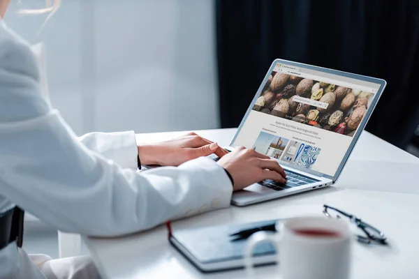 Ausgeschnittene Ansicht der Frau mit Laptop mit Hinterlegungsfotos Website auf dem Bildschirm am Schreibtisch — Stockfoto