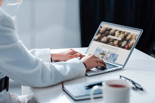 Cropped view of woman using laptop with depositphotos website on screen at office desk — Stock Photo