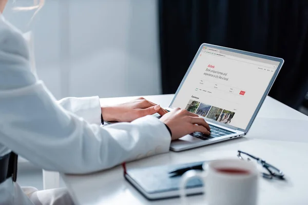 Cropped view of woman using laptop with airbnb website on screen at office desk — Stock Photo