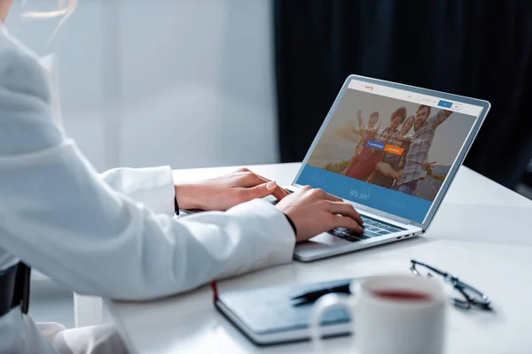 Cropped view of woman using laptop with couchsurfing website on screen at office desk — Stock Photo