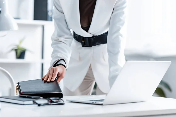 Обрізаний вид бізнес-леді в офіційному носінні тримає блокнот за комп'ютерним столом — стокове фото