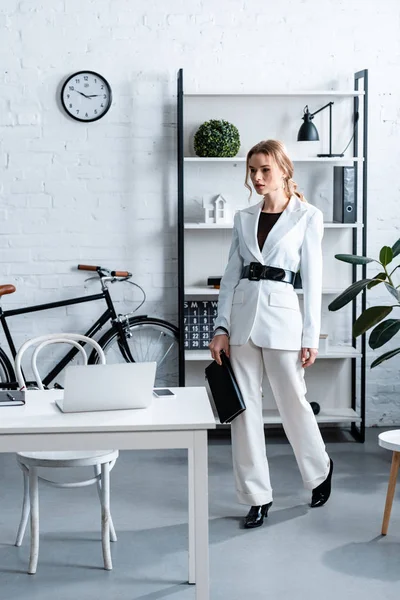 Seriöse Geschäftsfrau in weißer Festkleidung mit Notizbuch im modernen Bürointerieur — Stockfoto