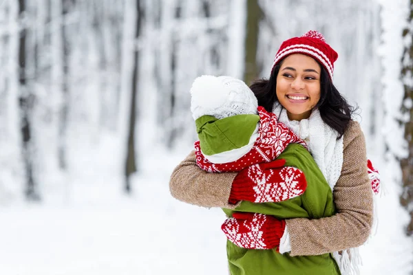 Atractiva afroamericana mujer abrazando hija en invierno parque - foto de stock