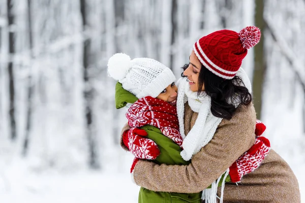 Sonriente afroamericano madre e hija abrazándose en invierno parque - foto de stock