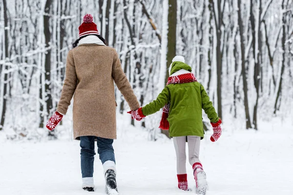 Madre e hija caminando y tomados de la mano en el parque de invierno - foto de stock