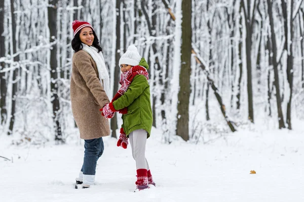 Afrikanisch-amerikanische Mutter und Tochter, lächelnd, Händchen haltend und in die Kamera blickend im Winterpark — Stockfoto