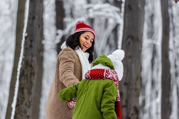 Africano americano mamá sonriendo y mirando preadolescente hija en invierno parque - foto de stock