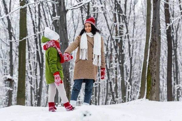 African american woman and preteen daughter walking, holding hands and looking at each other in winter park — Stock Photo