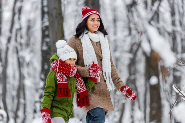 Hermosa mujer afroamericana y lindo niño preadolescente sonriendo y caminando en el parque de invierno - foto de stock