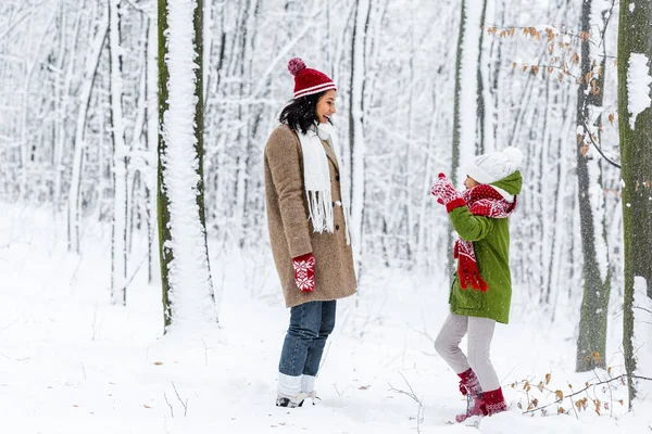 Fröhliche afrikanisch-amerikanische Mutter blickt Tochter mit erhobenen Händen im Winterpark an — Stockfoto