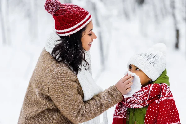 Beautiful african american woman wiping with napkin nose of preteen daughter in winter park — Stock Photo