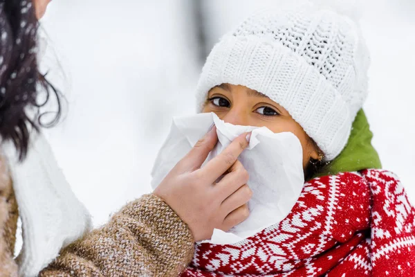 Vue recadrée de la mère essuyant avec le nez de serviette de fille mignonne dans le parc d'hiver — Photo de stock