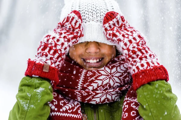 Mignon enfant afro-américain avec chapeau tricoté tiré sur les yeux souriant pendant les chutes de neige — Photo de stock