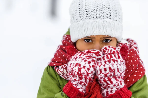 Vista de cerca del niño afroamericano en sombrero de punto, mitones y bufanda mirando a la cámara en invierno - foto de stock