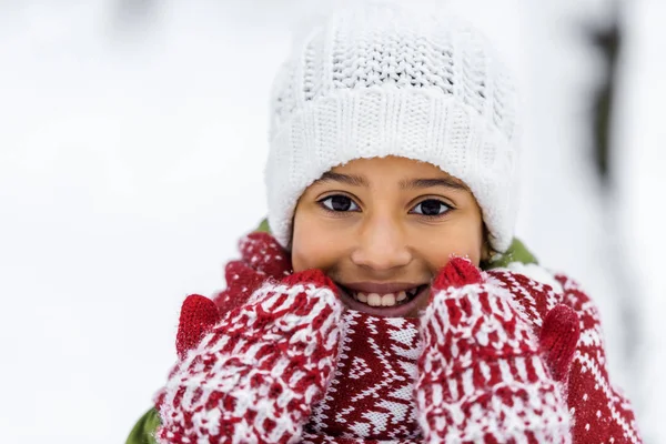 Close up view of african american child in knitted hat, mittens and scarf smiling and looking at camera in winter — Stock Photo