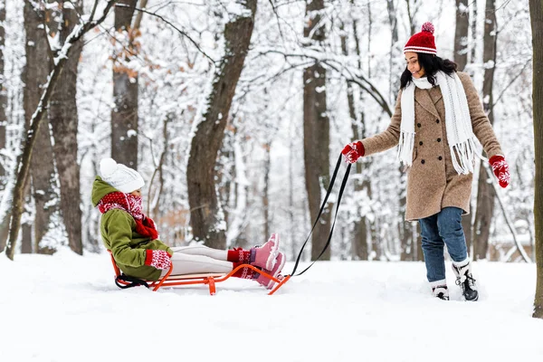 Attractive african american woman pulling daughter on sledge in winter park — Stock Photo
