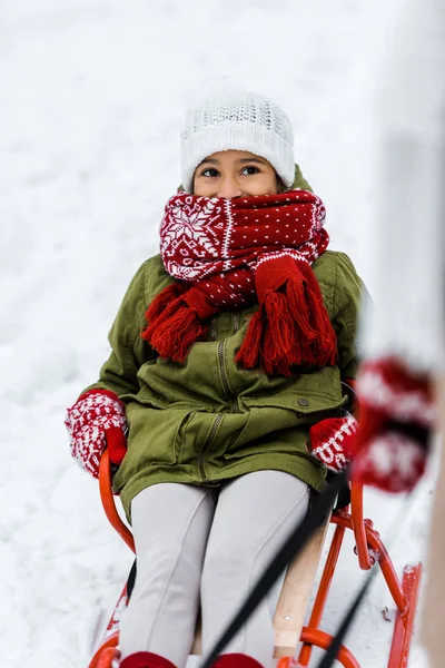 Africano americano niño en trineo mirando mujer en nieve fondo - foto de stock