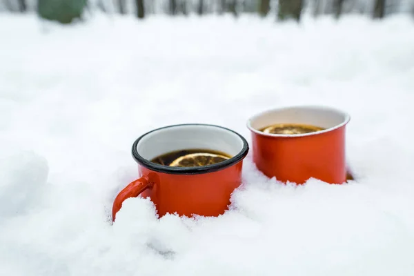 Две чашки чая с лимонами, стоящими на белом снегу возле деревьев в снежном лесу — стоковое фото