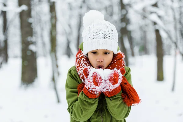 Carino afroamericano bambino soffiando neve nella foresta invernale — Foto stock