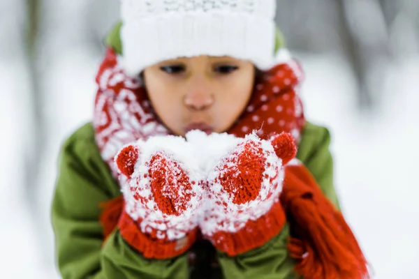 Cute african american child blowing white snow in winter forest — Stock Photo