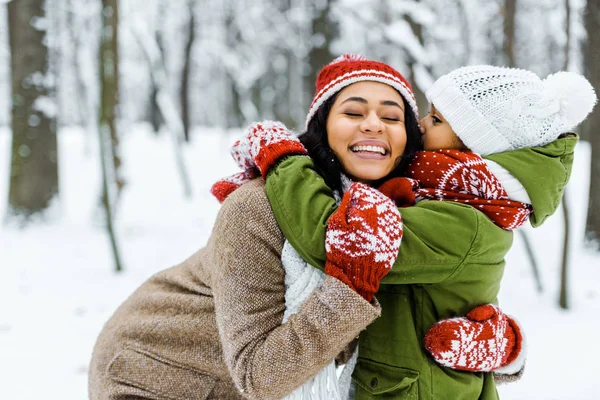 Süße afrikanisch-amerikanische Tochter umarmt Mutter im Winterwald — Stockfoto