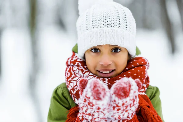 Süße afrikanisch-amerikanische Kind zeigt weißen Schnee vor der Kamera im Winterwald — Stockfoto