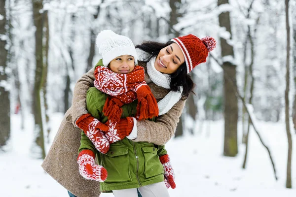 Attractive african american mother hugging cute preteen daughter in winter forest — Stock Photo