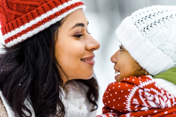 Attractive african american mother smiling and looking at cute preteen daughter in winter forest — Stock Photo