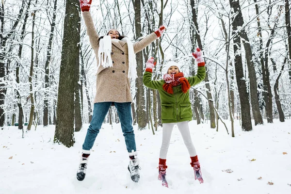 Attractive african american mother and cute preteen daughter  jumping up in winter forest — Stock Photo