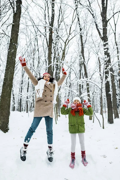 Atractivo africano americano madre y lindo preadolescente hija saltar hasta en invierno bosque - foto de stock