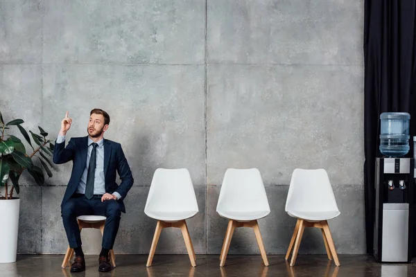 Hombre de negocios en traje mostrando gesto de idea y sentado en la sala de espera - foto de stock