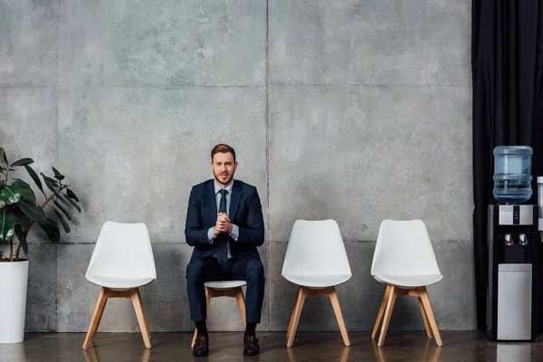 Geschäftsmann im Anzug mit gefalteten Händen sitzt in Wartehalle und blickt in die Kamera — Stockfoto