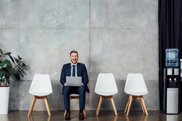 Allegro uomo d'affari seduto sulla sedia e utilizzando il computer portatile in sala d'attesa — Foto stock