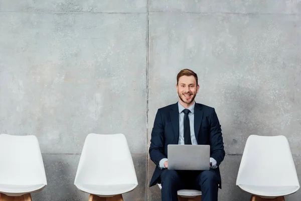 Усміхнений бізнесмен сидить на стільці і використовує ноутбук у залі очікування — стокове фото