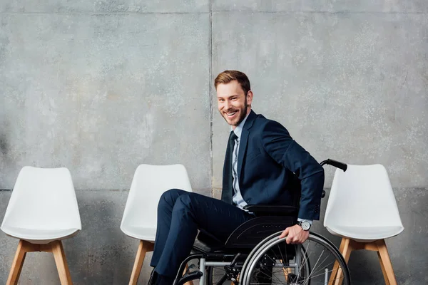Lächelnder Geschäftsmann sitzt im Rollstuhl in Wartehalle und blickt in die Kamera — Stockfoto