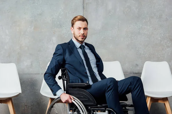 Schöner Geschäftsmann sitzt im Rollstuhl in Wartehalle und blickt in die Kamera — Stockfoto