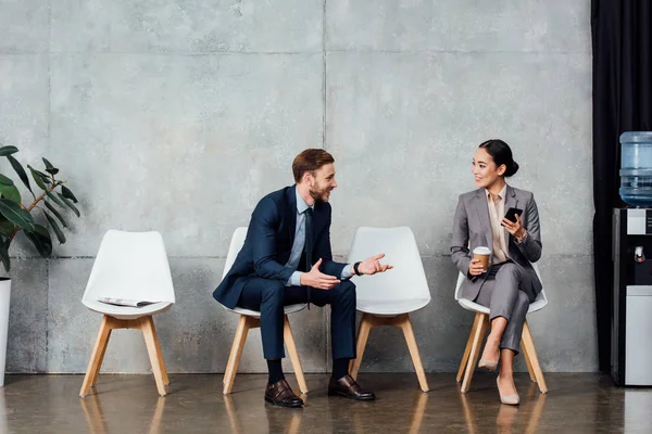 Handsome businessman talking to asian businesswoman in waiting hall — Stock Photo