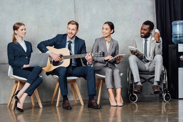 Multicultural businesspeople using digital devices while businessman playing acoustic guitar in waiting hall — Stock Photo