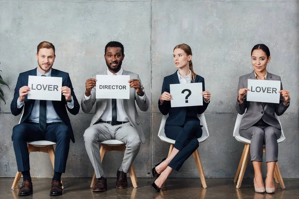 Multiethnic businesspeople holding cards with 'lover', 'director' words and question mark in waiting hall — Stock Photo